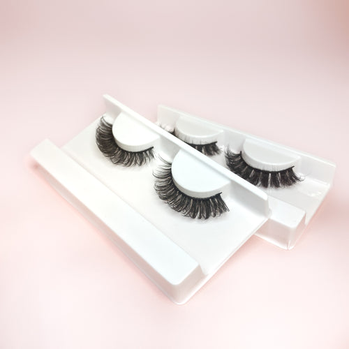 Two pairs of false strip lashes that resemble extensions, displayed in white trays on a pink background.